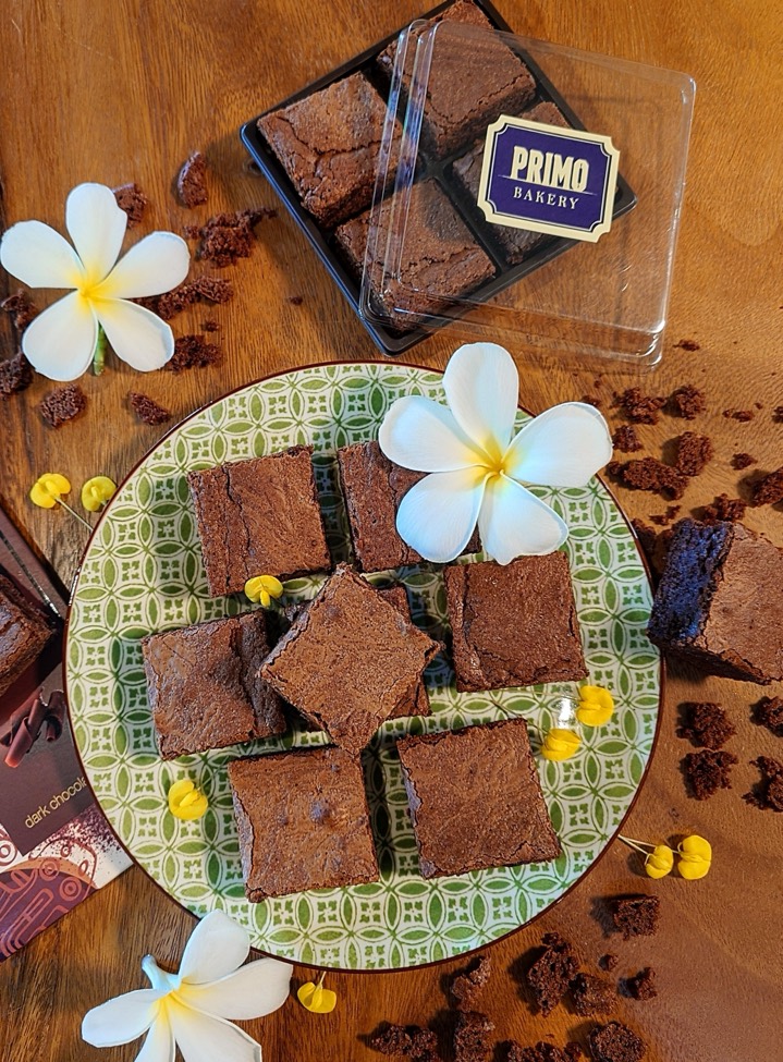 Fudgy brownies on a plate beside a gift box with a navy Primo Bakery label